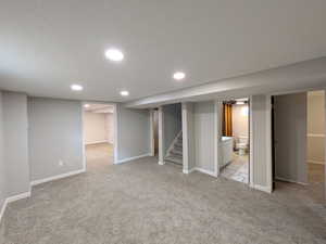 Finished below grade area featuring light colored carpet, stairs, a textured ceiling, and recessed lighting