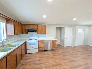 Kitchen with appliances with stainless steel finishes, brown cabinetry, light countertops, light wood-style flooring, and recessed lighting