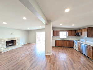 Kitchen featuring light countertops, a fireplace, appliances with stainless steel finishes, open floor plan, and light wood-type flooring