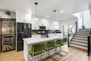 Kitchen featuring white cabinets, appliances with stainless steel finishes, hanging light fixtures, a breakfast bar, and a kitchen island with sink