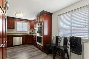 Kitchen with stainless steel appliances, dark wood-type flooring, dark brown cabinets, and light stone countertops