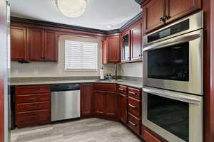 Kitchen with stainless steel appliances, reddish brown cabinets, dark stone counters, and light wood-type flooring