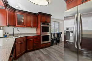 Kitchen with stainless steel appliances, light stone counters, glass insert cabinets, reddish brown cabinets, and light wood-type flooring