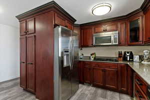 Kitchen with stainless steel appliances, dark stone countertops, light wood-type flooring, glass insert cabinets, and dark brown cabinets