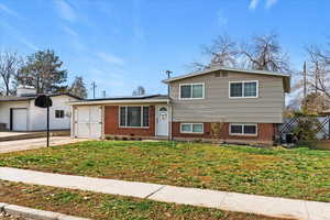 Tri-level home featuring solar panels, brick siding, and a front yard