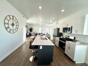 Kitchen with open floor plan, stainless steel appliances, a kitchen bar, a center island with sink, and white cabinets