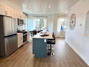 Kitchen with appliances with stainless steel finishes, a breakfast bar area, a textured ceiling, white cabinetry, and a kitchen island with sink