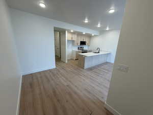 Kitchen with a peninsula, stainless steel appliances, light wood-type flooring, open floor plan, and a breakfast bar