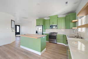 Kitchen featuring open shelves, green cabinetry, wood counters, stainless steel appliances, and a kitchen island