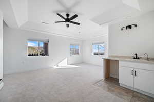 Unfurnished living room featuring light colored carpet, a raised ceiling, plenty of natural light, and a ceiling fan