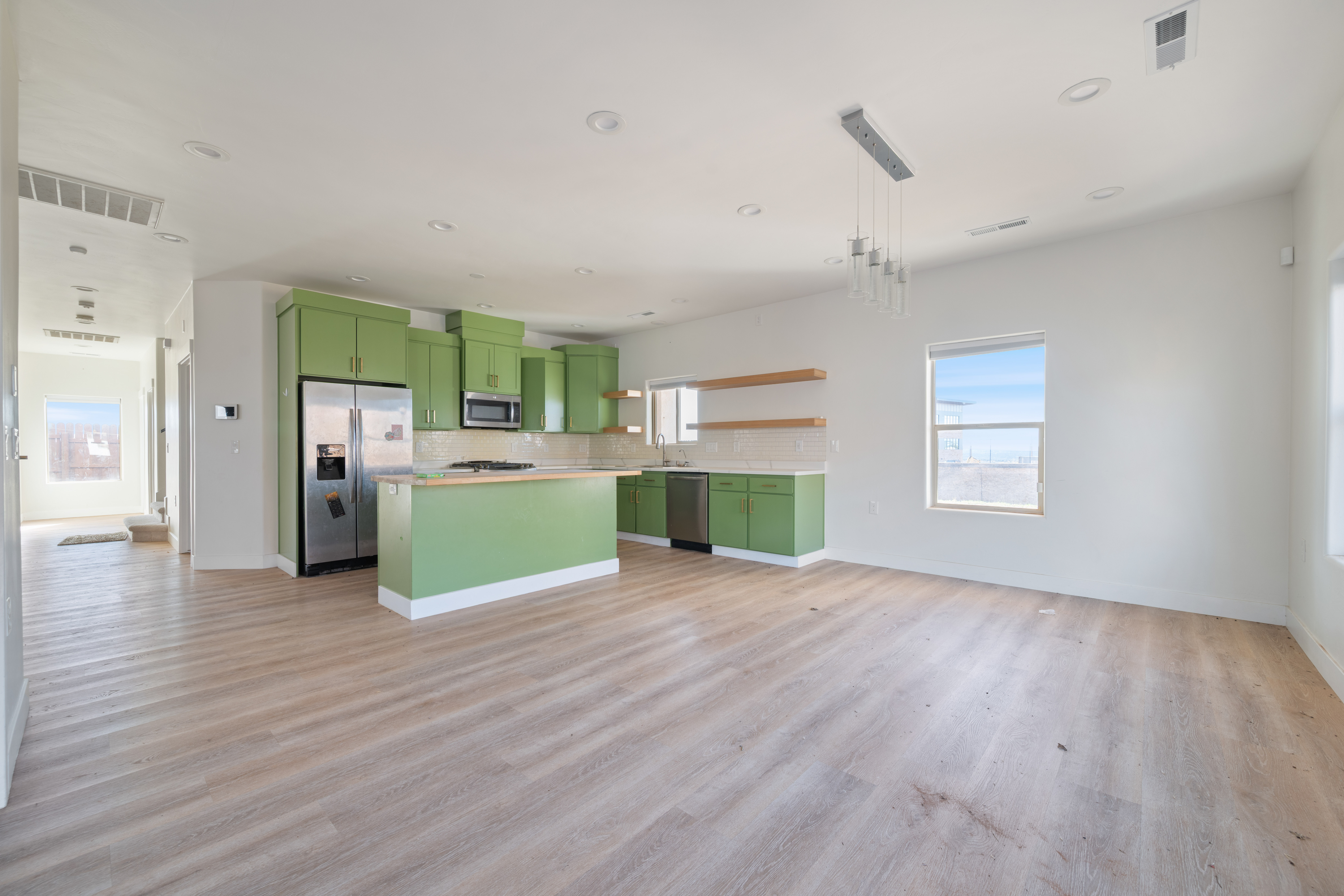 Kitchen featuring green cabinetry, backsplash, appliances with stainless steel finishes, light countertops, and open floor plan