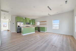 Kitchen featuring green cabinetry, backsplash, appliances with stainless steel finishes, light countertops, and open floor plan