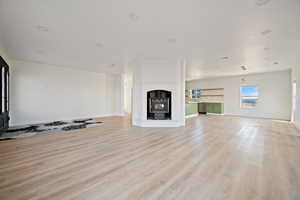 Unfurnished living room featuring light wood-style floors, a fireplace with raised hearth, and recessed lighting