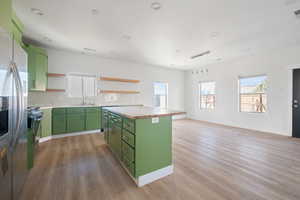 Kitchen with green cabinetry, open shelves, a center island, stainless steel appliances, and hanging light fixtures