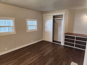 Unfurnished bedroom with a decorative wall, dark wood-style floors, and a closet