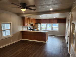 Kitchen featuring brown cabinetry, light countertops, a peninsula, dark wood-style floors, and a textured ceiling