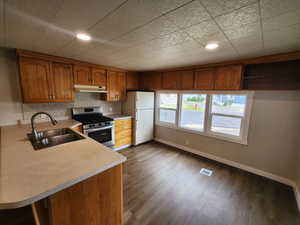 Kitchen featuring brown cabinets, stainless steel gas range oven, freestanding refrigerator, light countertops, and dark wood-type flooring