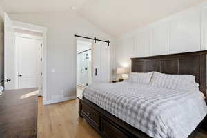 Bedroom featuring vaulted ceiling, a barn door, and light wood-style flooring