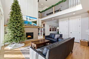 Living area with a towering ceiling, a fireplace, light wood-style flooring, and recessed lighting