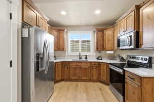 Kitchen featuring stainless steel appliances, light wood-type flooring, brown cabinets, recessed lighting, and light stone countertops
