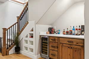 Indoor dry bar featuring brown cabinetry, wine cooler, light wood finished floors, and stairway