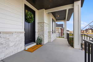 View of exterior entry featuring covered porch, stone siding, and a residential view