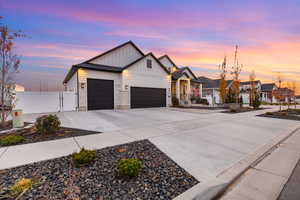 Modern farmhouse with board and batten siding, concrete driveway, an attached garage, and a gate