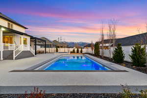Pool at dusk featuring a fenced backyard, a patio area, and a residential view