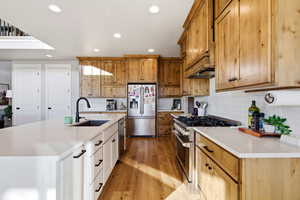 Kitchen with stainless steel appliances, light stone countertops, light wood-type flooring, an island with sink, and white cabinetry