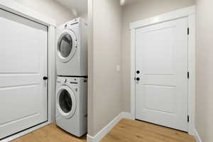Laundry area featuring light wood-style flooring and stacked washer / drying machine with door to utility room