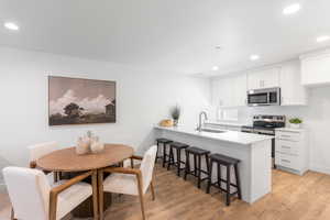 Kitchen featuring recessed lighting, white cabinetry, stainless steel appliances, a kitchen bar, and a peninsula
