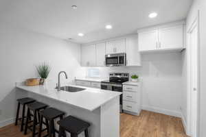 Kitchen featuring white cabinets, a breakfast bar, stainless steel appliances, a peninsula, and light stone counters