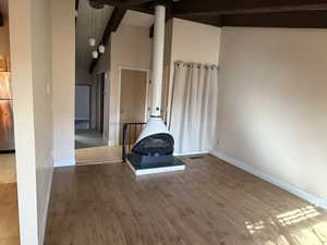 Unfurnished living room with high vaulted ceiling, light wood-style floors, beam ceiling, and a wood stove
