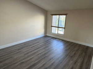 Unfurnished room featuring dark wood finished floors and vaulted ceiling
