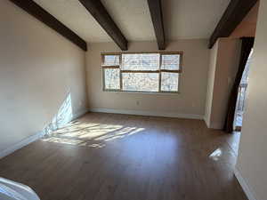 Unfurnished living room with a textured ceiling, wood finished floors, and beamed ceiling