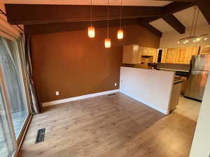 Kitchen with dark countertops, freestanding refrigerator, beamed ceiling, light wood finished floors, and a peninsula