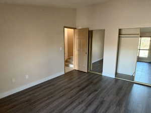 Unfurnished bedroom with vaulted ceiling, dark wood-type flooring, and multiple closets