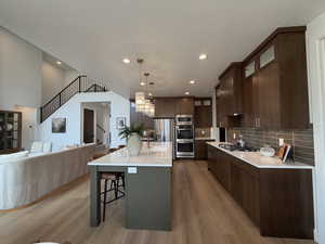 Kitchen with light stone counters, hanging light fixtures, glass fronted cabinets, light wood-type flooring, and dark wood finish cabinets