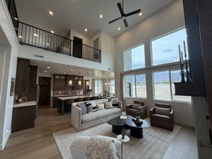 Living area with light wood-style floors, a ceiling fan, suspended lighting, and a high ceiling