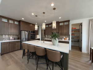 Kitchen with glass fronted cabinets, dark wood finish cabinets, a center island with sink, and light stone counters