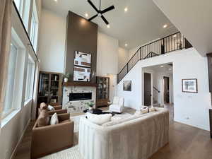 Living room with a ceiling fan, a high end fireplace, a high ceiling, dark wood-type flooring, and recessed lighting