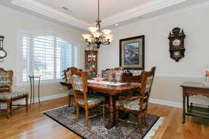 Dining space with crown molding, a chandelier, light wood-style flooring, and a tray ceiling