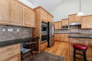 Kitchen featuring backsplash, light brown cabinets, stainless steel appliances, dark stone countertops, and light wood-type flooring