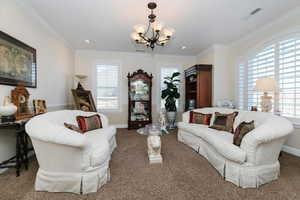 Living room featuring carpet flooring, crown molding, and a chandelier