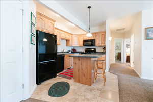 Kitchen with black appliances, light brown cabinets, a kitchen island, a breakfast bar area, and pendant lighting
