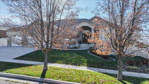 View of property hidden behind natural elements featuring a front lawn, concrete driveway, stucco siding, and a garage