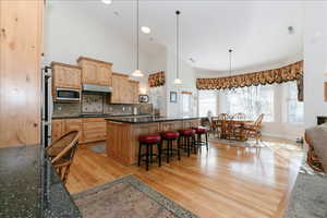 Kitchen featuring high vaulted ceiling, decorative light fixtures, light wood finished floors, a breakfast bar area, and stainless steel microwave