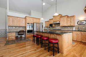 Kitchen featuring pendant lighting, backsplash, light brown cabinets, high vaulted ceiling, and an island with sink