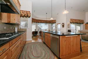 Kitchen featuring exhaust hood, dark stone counters, stainless steel appliances, decorative light fixtures, and lofted ceiling