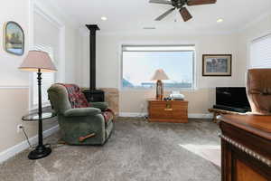 Sitting room with a wood stove, ornamental molding, plenty of natural light, carpet floors, and a ceiling fan